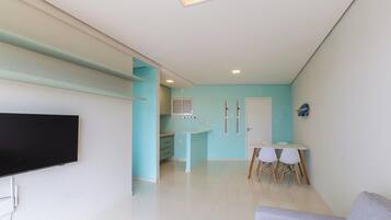 Ein modernes Wohnzimmer mit einem Flachbildfernseher, einem Essbereich mit Tisch und Stühlen sowie einer Küche mit Schränken und einem Fenster.
