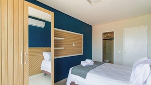 Quarto com cama, guarda-roupa, espelho e banheiro visível por uma porta aberta.