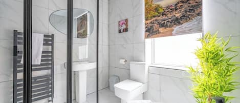 Un baño moderno con cabina de ducha de vidrio, un lavamanos blanco, un inodoro y una bañera.