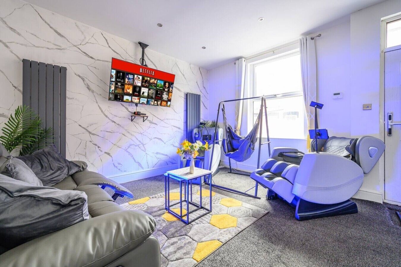 Een moderne woonkamer met een bank, een massagestoel, een hangstoel en een Netflix-scherm aan de muur.