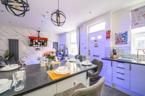 Et moderne køkken med marmorbeklædt bagvæg, et spiseområde med et bord dækket til fire personer og en køkkenø med vask og barpladser.