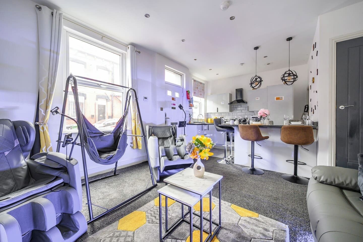 A modern living room with a sofa, a hanging chair, a coffee table, and a kitchen area with bar stools.
