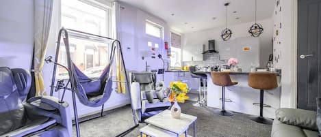 Una sala de estar moderna con un sofá, una silla colgante, una mesa de centro y una zona de cocina con taburetes de bar.