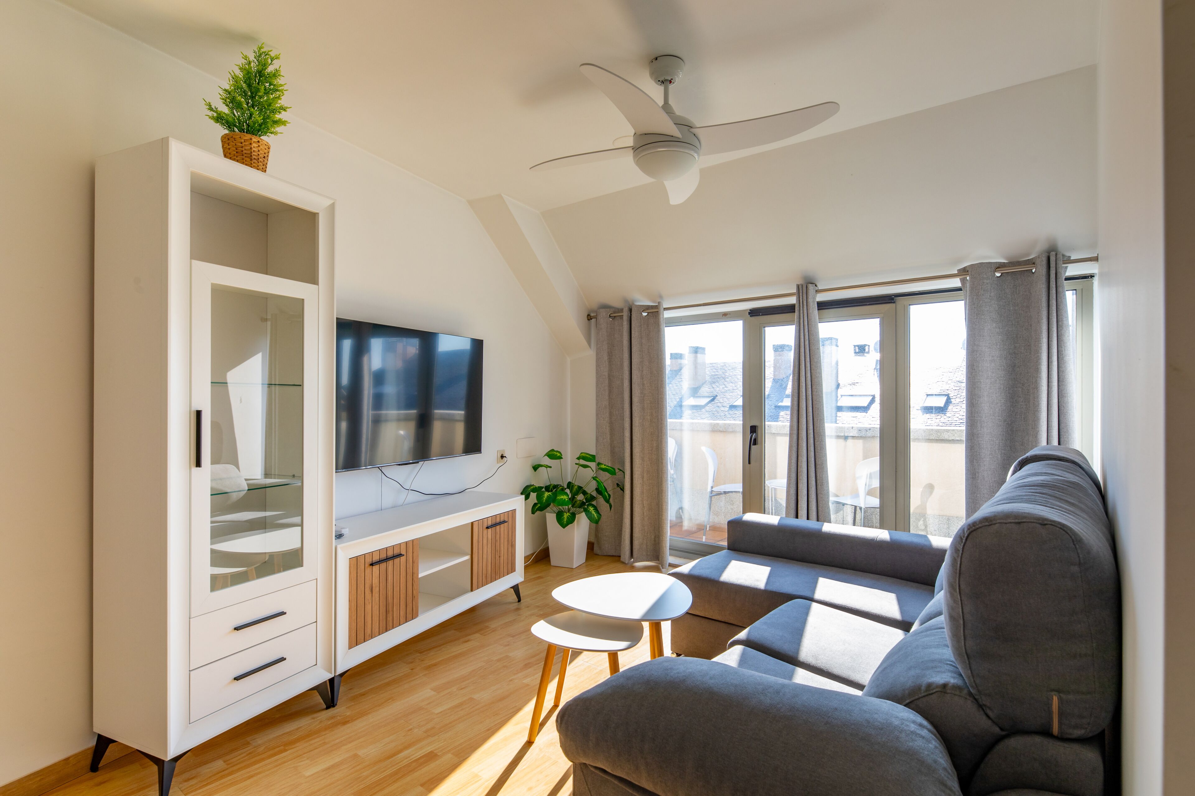 A modern living room with a flat-screen TV, a sofa, a small table, and a ceiling fan.