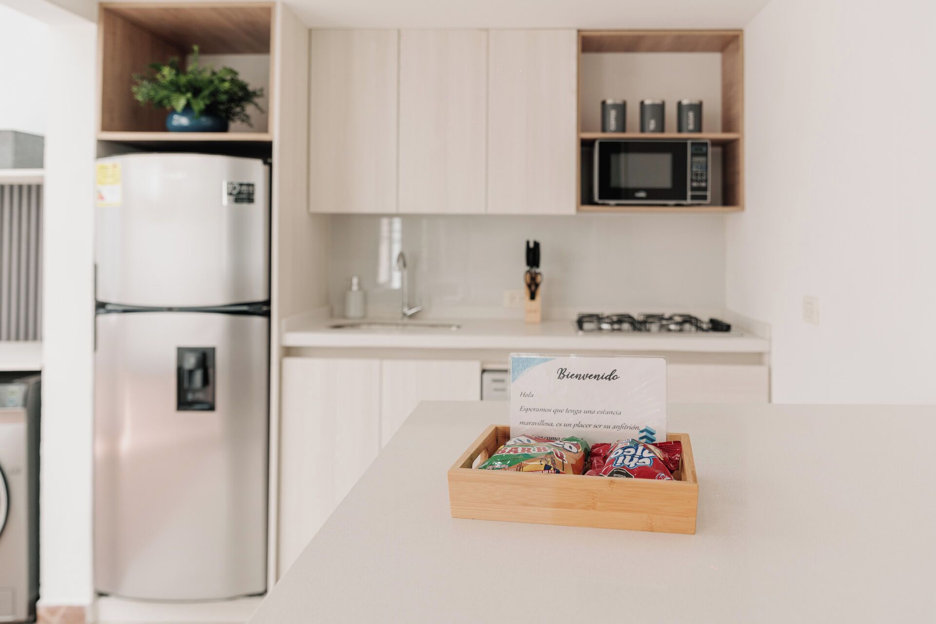 A kitchen with a refrigerator, microwave, and a wooden box with snacks on the counter.