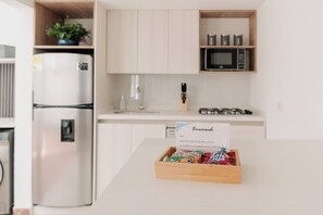 A kitchen with a refrigerator, microwave, and a wooden box with snacks on the counter.
