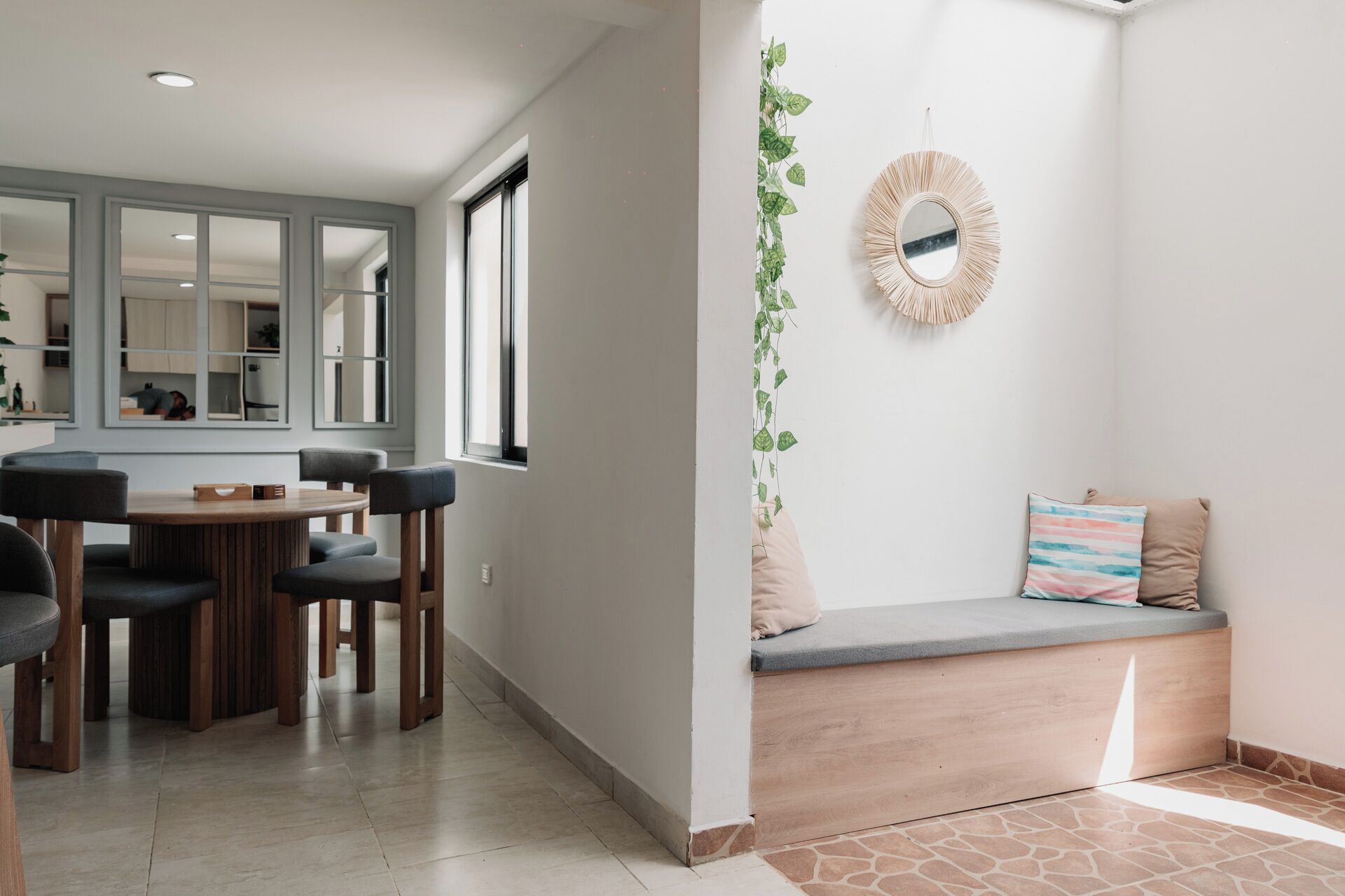 A modern interior with a dining area, a bench with cushions, and a wall-mounted mirror.