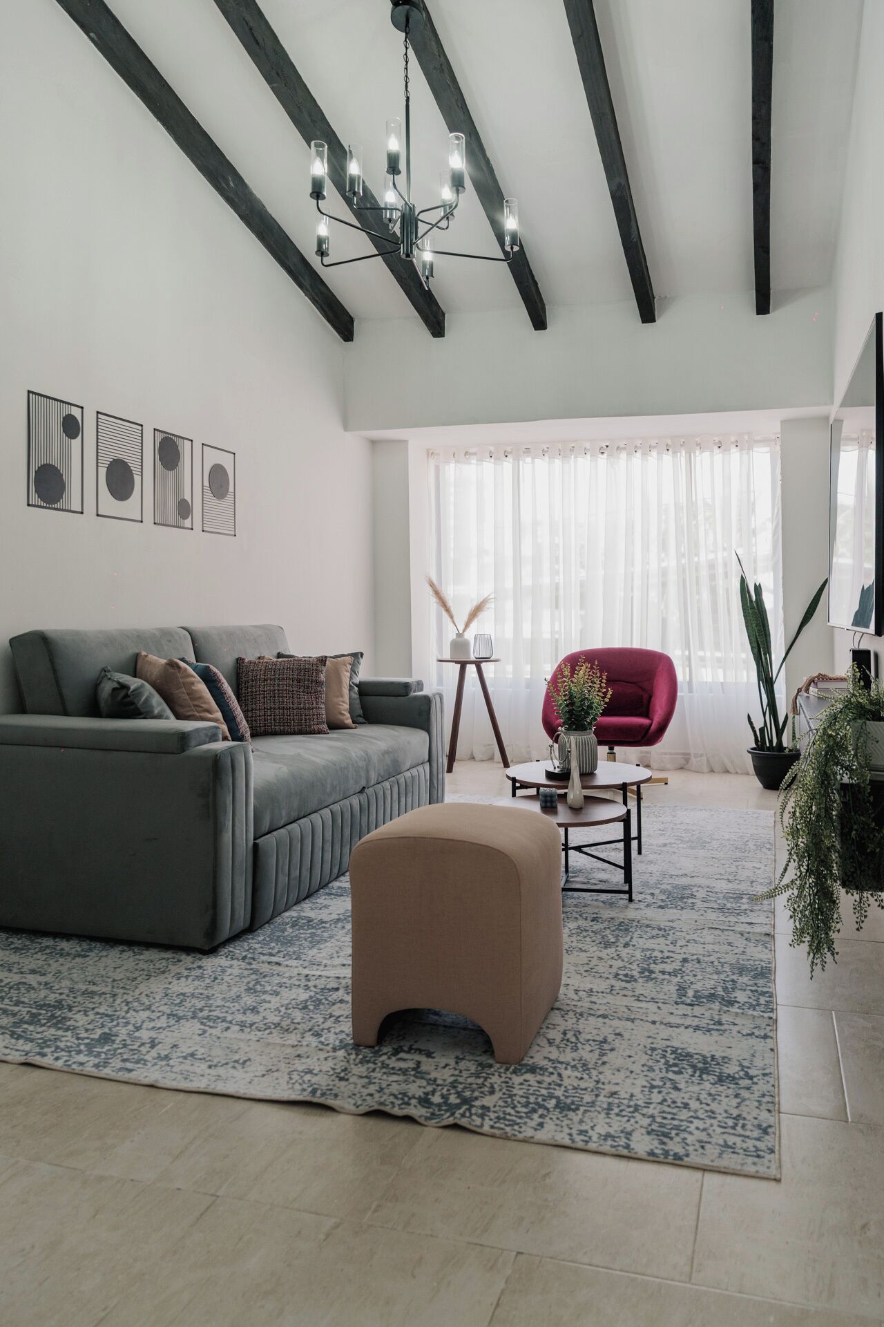 A modern living room with a grey sofa, a red chair, a coffee table, and a chandelier.