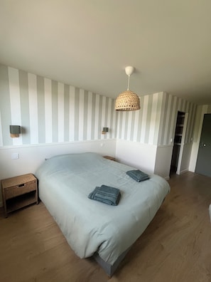 Een slaapkamer met een groot bed, gestreepte wanden, een hanglamp en een klein houten nachtkastje.