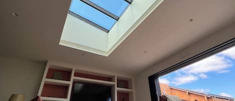 Una sala de estar moderna con tragaluz, televisor de pantalla plana y dos sofás.