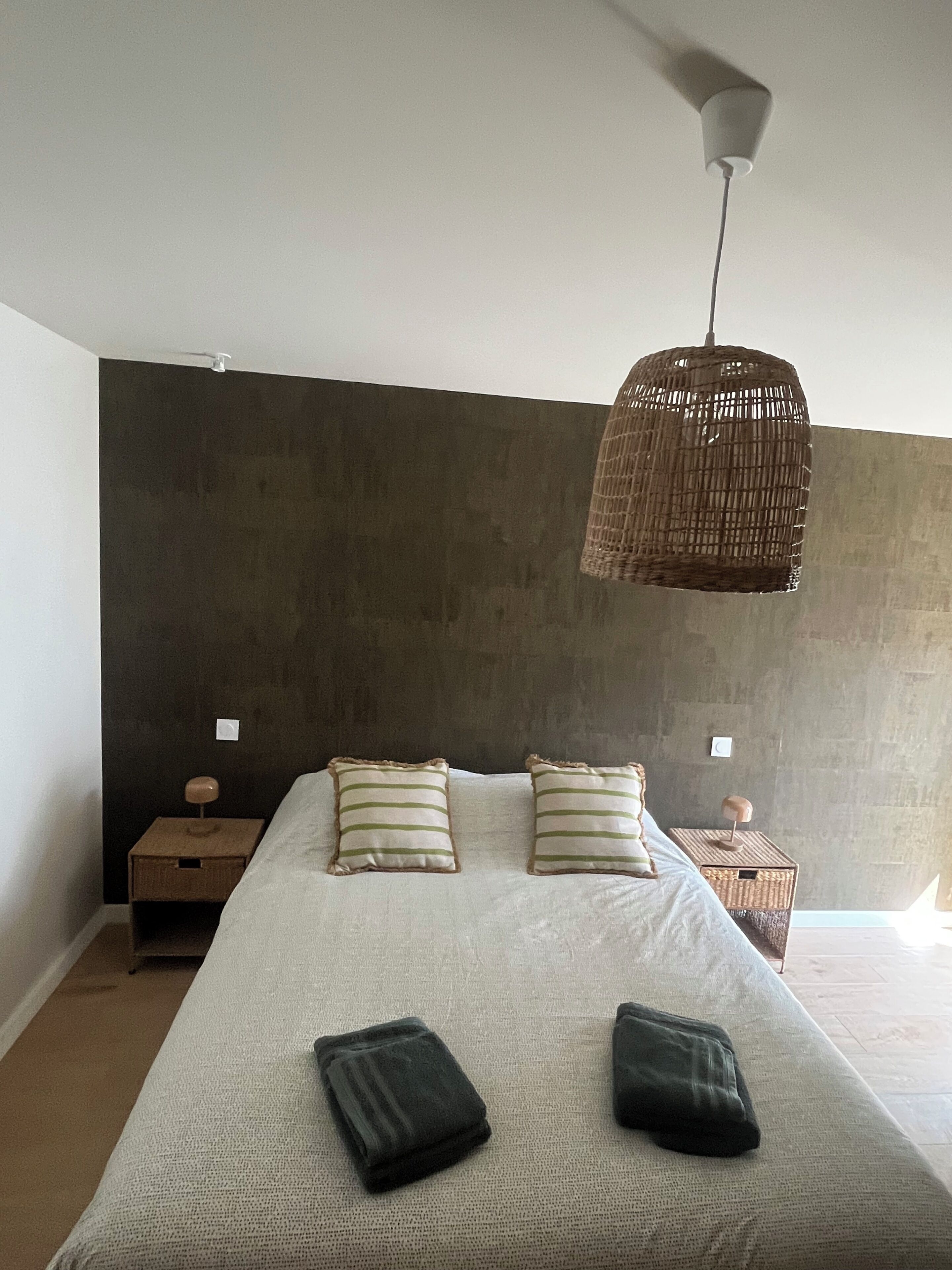 A bedroom with a large bed, two bedside tables, a hanging light fixture, and a dark wall.