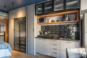 Eine moderne Küche mit Mikrowelle, Kaffeemaschine und Toaster auf der Arbeitsplatte, einem Glastürenschrank und einem Holzregal über der Spüle.