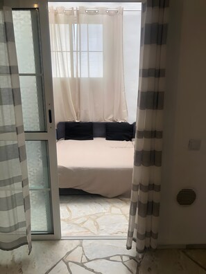 Un dormitori amb llit, cortines, finestra i porta.
