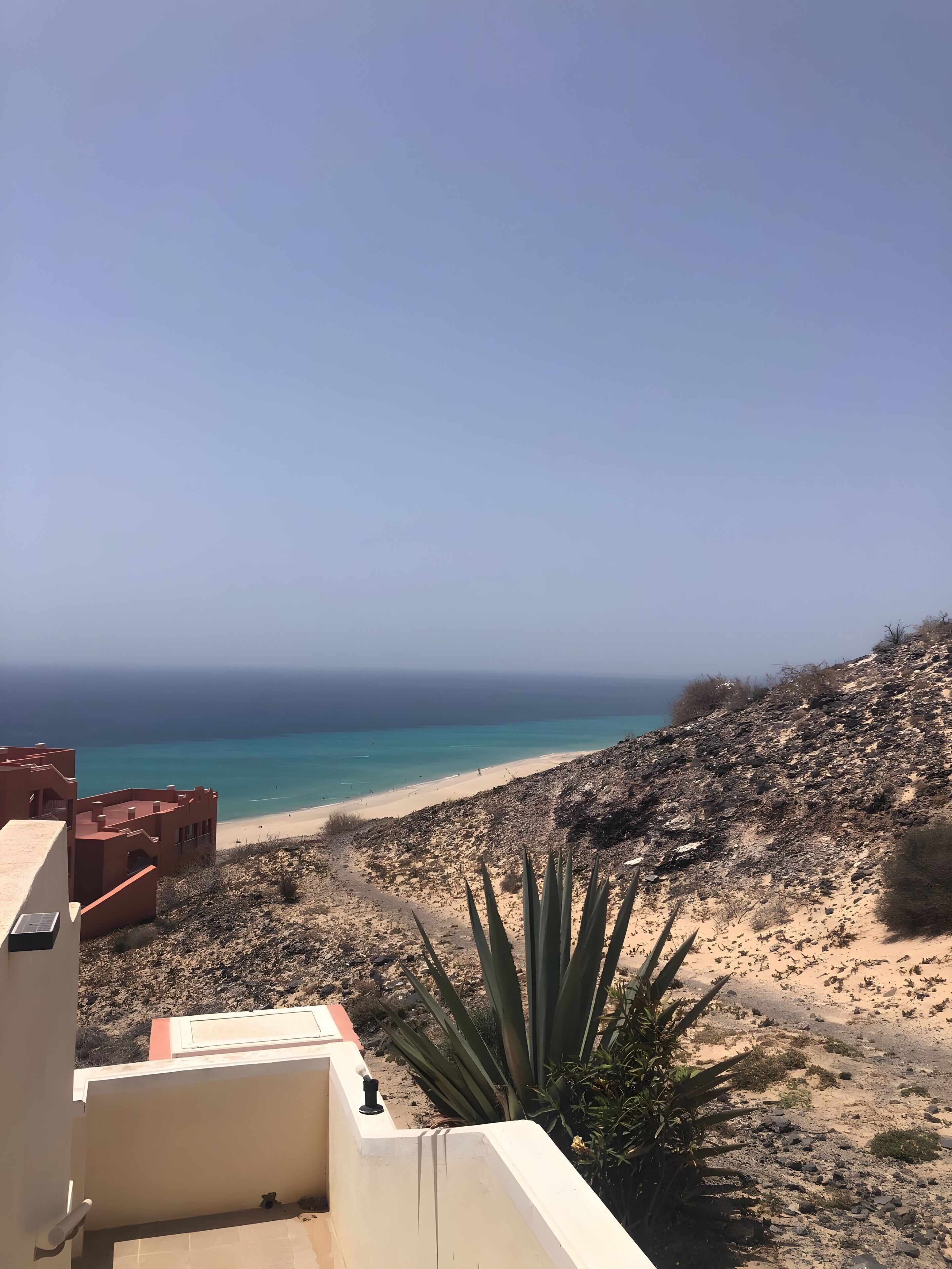 Une vue sur la côte, avec une plage de sable, un ciel dégagé et une colline rocheuse.