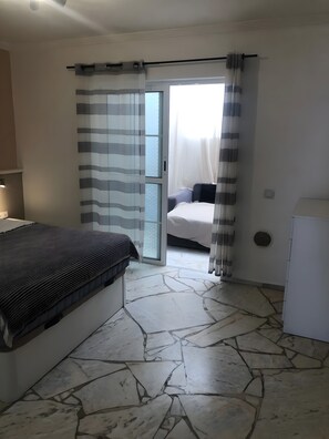 Une chambre à coucher avec un lit, une fenêtre avec des rideaux, une porte donnant sur l’extérieur et un radiateur blanc.