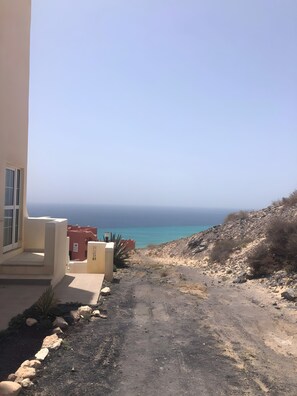 Un edifici amb vistes al mar, un camí de terra i algunes roques.
