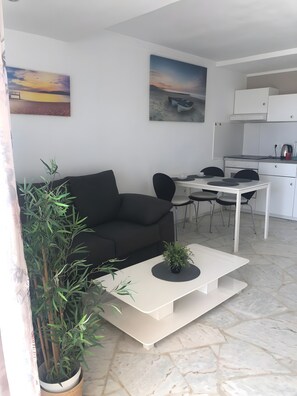Un saló modern amb un sofà negre, una taula de dinar amb caires, una cuina amb armaris i dos quadres penjats a la paret.