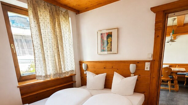Une chambre à coucher avec un lit en bois, une fenêtre avec des rideaux, un tableau au mur et un plafond en bois.