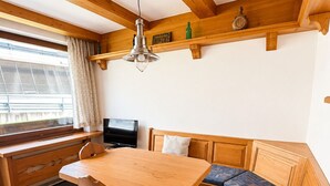 Un coin repas en bois avec une table et des bancs, un téléviseur et une fenêtre avec des stores.
