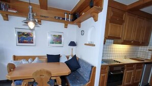 Une cuisine compacte avec des meubles en bois, un four encastré et un coin repas comprenant une table et un banc en bois.