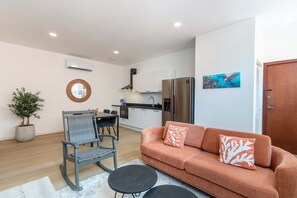 A modern living room with a sofa, a dining table with chairs, a kitchen area with a refrigerator, and a potted plant. - Elegant Apartment in Historic Punda (Willemstad)