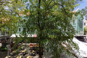 A tree-lined courtyard with outdoor seating and a building with green and white facades. - Elegant Apartment in Historic Punda (Willemstad)