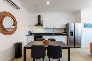 A modern kitchen with white cabinets, a black countertop, and a stainless steel refrigerator. - Elegant Apartment in Historic Punda (Willemstad)