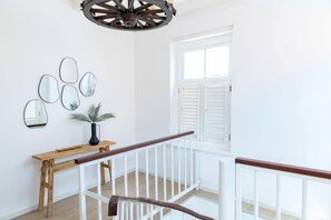 A staircase with a wooden handrail and white balusters, leading to a landing with a white wall and a window with white shutters. - Elegant Apartment in Historic Punda (Willemstad)