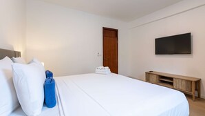 Ein Hotelzimmer mit einem Bett, einem Nachttisch aus Holz, einem an der Wand befestigten Fernseher und einer Tür.