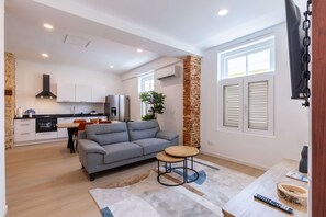 A modern interior with a grey sofa, a small round table, and a kitchen area with white cabinets and a black range hood. - History Comfort Character in Willemstad (Willemstad)