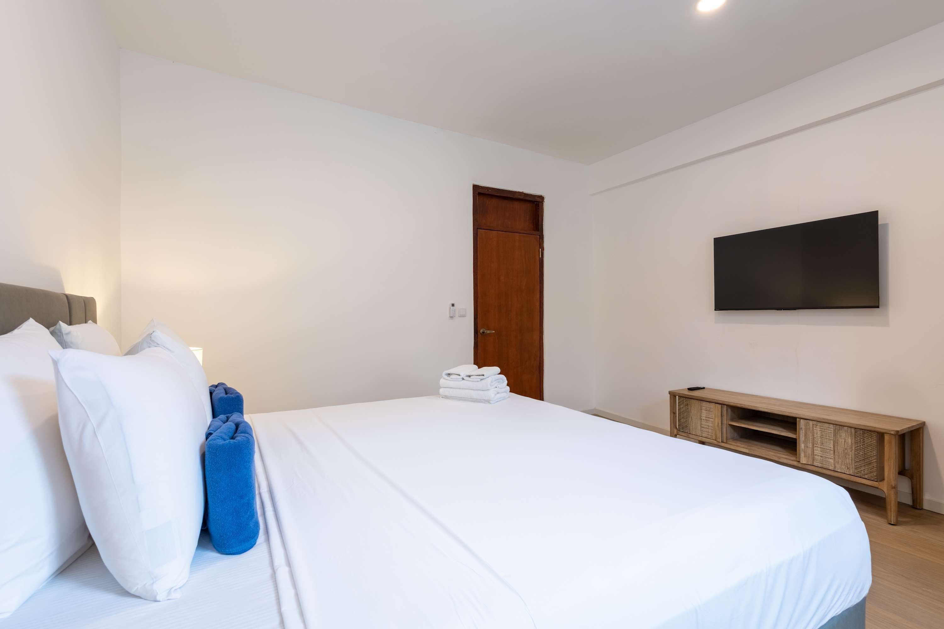 A hotel room with a bed, a wooden bedside table, a television mounted on the wall, and a door.