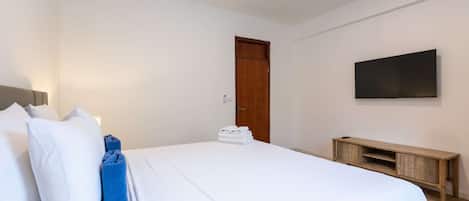 A hotel room with a bed, a wooden bedside table, a television mounted on the wall, and a door.