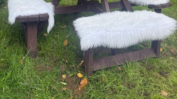 A picnic table with a vase of flowers and fluffy white cushions.