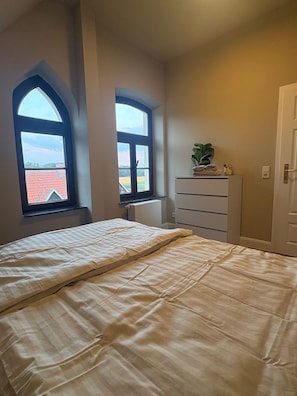 A bedroom with a bed, two windows, a dresser, and a door. - Apartment "Hof Hageneck" with Shared Terrace, Garden, and Wi-Fi (Everswinkel)