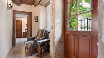 A hallway with a wooden door, a chair, and a view of greenery outside.