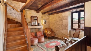 A rustic interior with a wooden staircase, stone walls, a fireplace, and a view through a window.