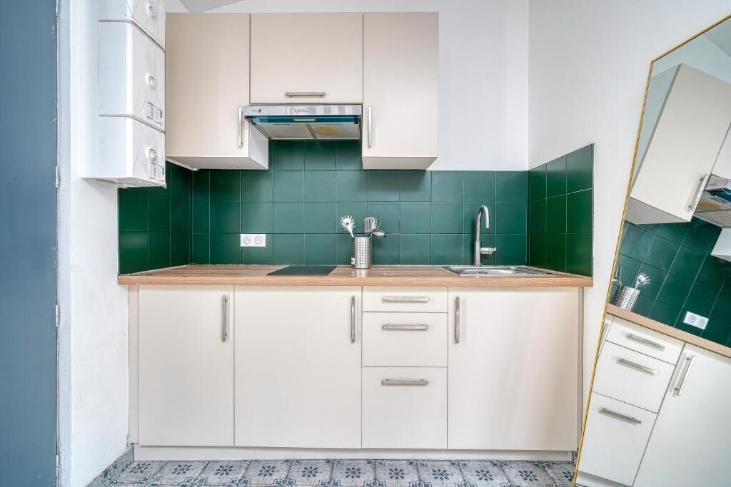 A compact kitchen with white cabinets, a stainless steel sink, and a green backsplash.