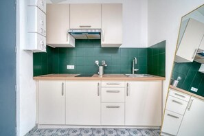 A compact kitchen with white cabinets, a stainless steel sink, and a green backsplash.