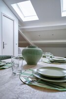 A dining table set with plates, glasses, and cutlery, a green vase, and a skylight above.
