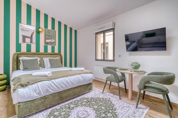 A bedroom with a bed, a desk, chairs, a TV, and striped walls.