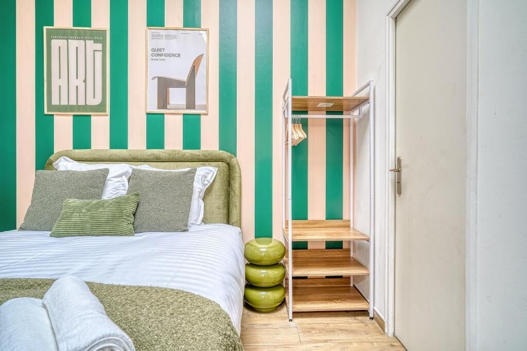 A bedroom with a bed, pillows, a framed picture, a shelf, and a wardrobe.