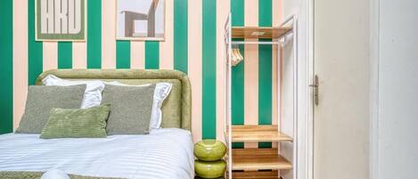 A bedroom with a bed, pillows, a framed picture, a shelf, and a wardrobe.