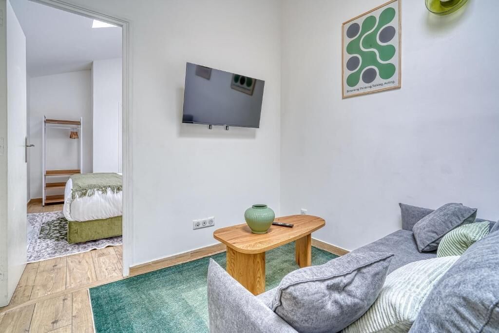 Een moderne woonkamer met een flatscreen televisie aan de muur, een houten salontafel en een groene vaas.