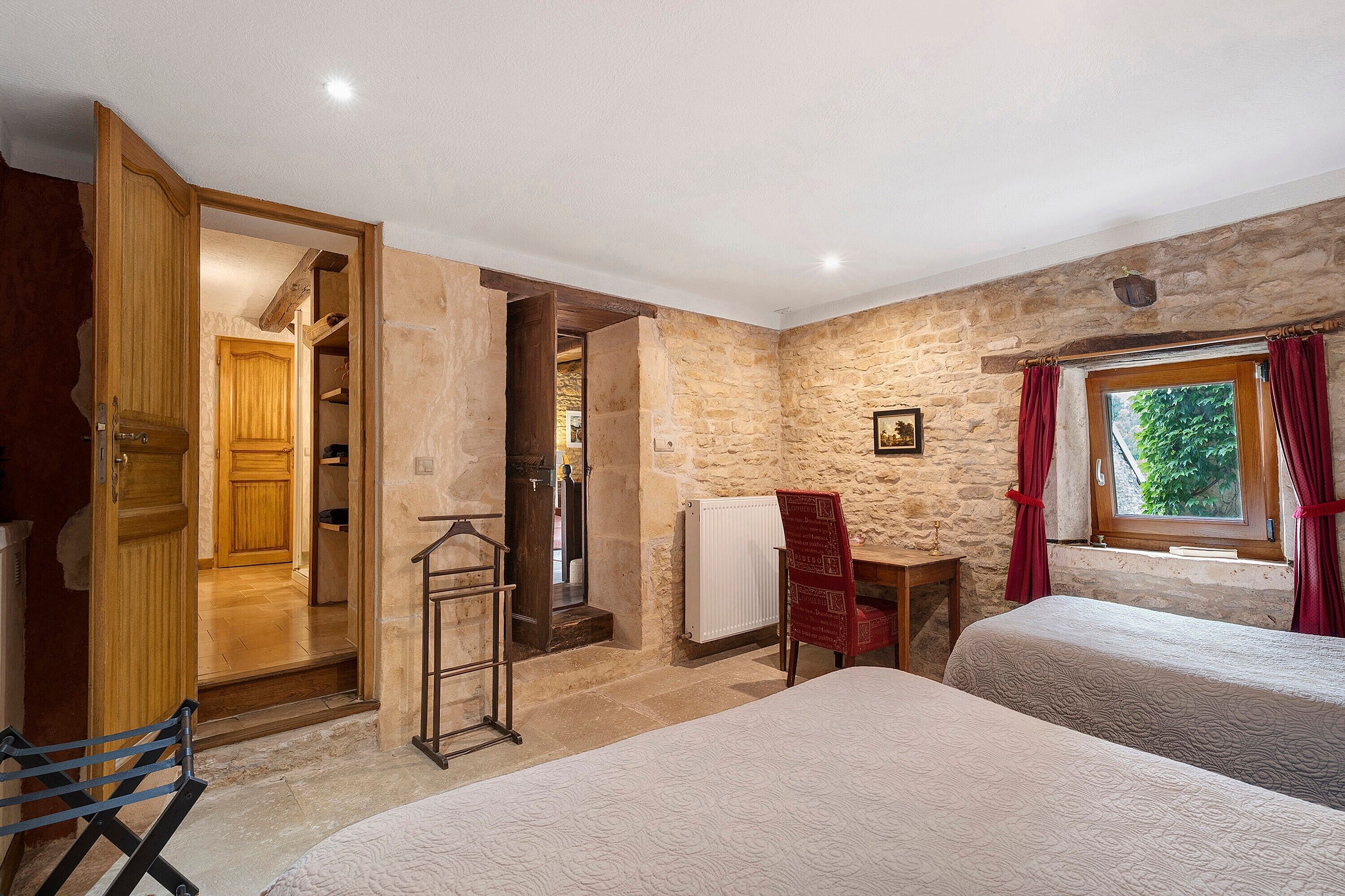 A bedroom with two beds, a wooden wardrobe, a radiator, and a window with curtains.