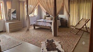 Un letto a baldacchino con struttura in legno e tende leggere, una panca in legno, un tavolino e uno specchio appeso al muro.