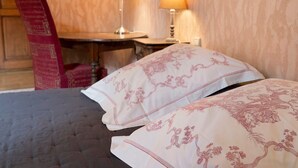 Habitación de hotel con cama, dos lámparas de noche, una mesa de madera y una silla roja.