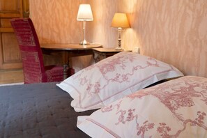 Habitación de hotel con cama, dos lámparas de noche, una mesa de madera y una silla roja.