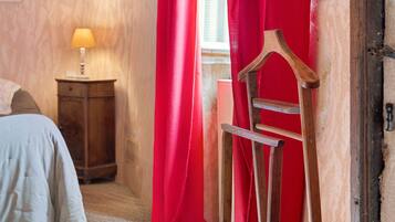 Een kamer met een houten stoel, een klein houten kastje en een bed met een witte spreidek.