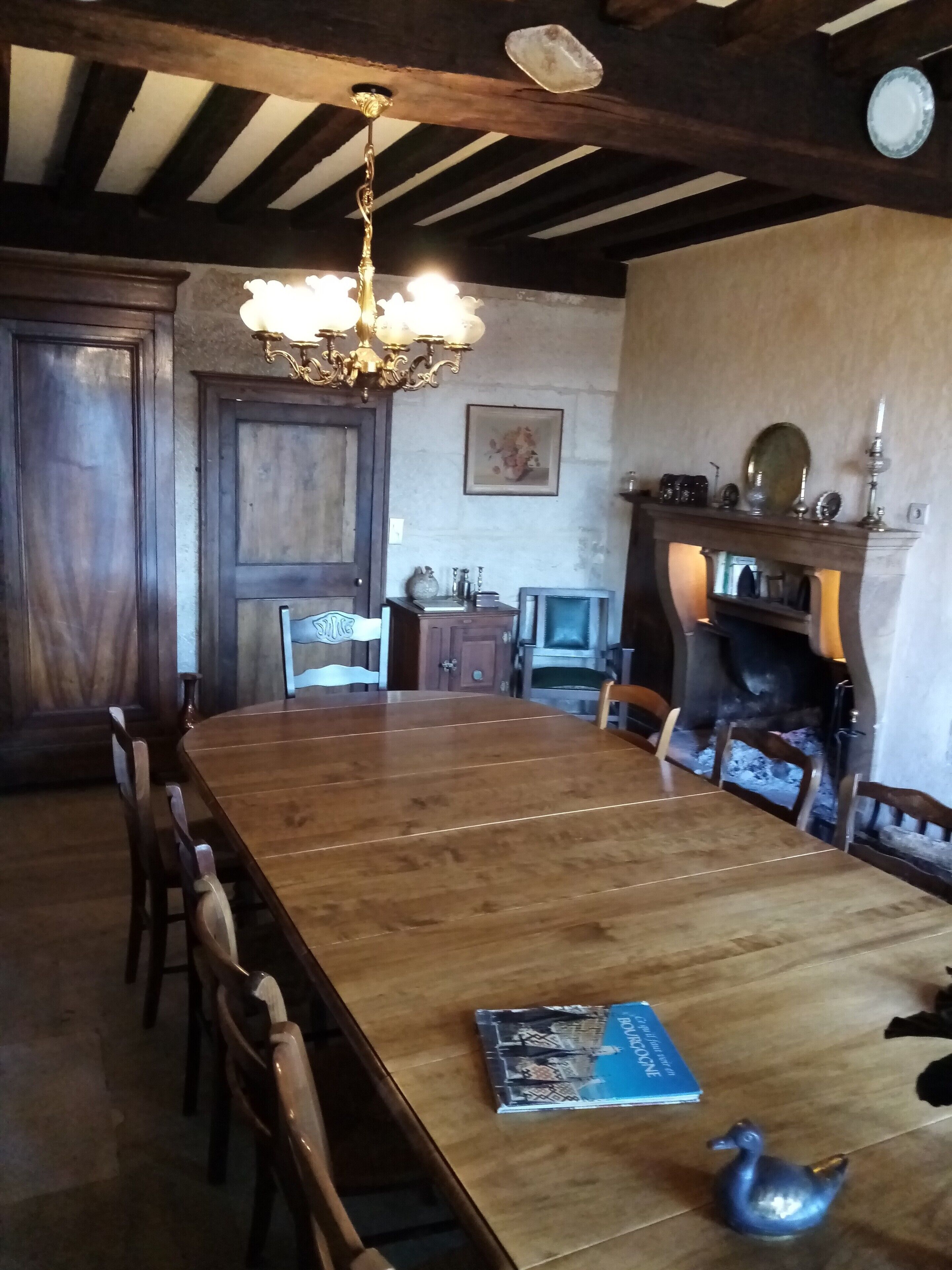 Een eethoek met een grote houten tafel, stoelen, een kroonluchter, een open haard en een televisie.