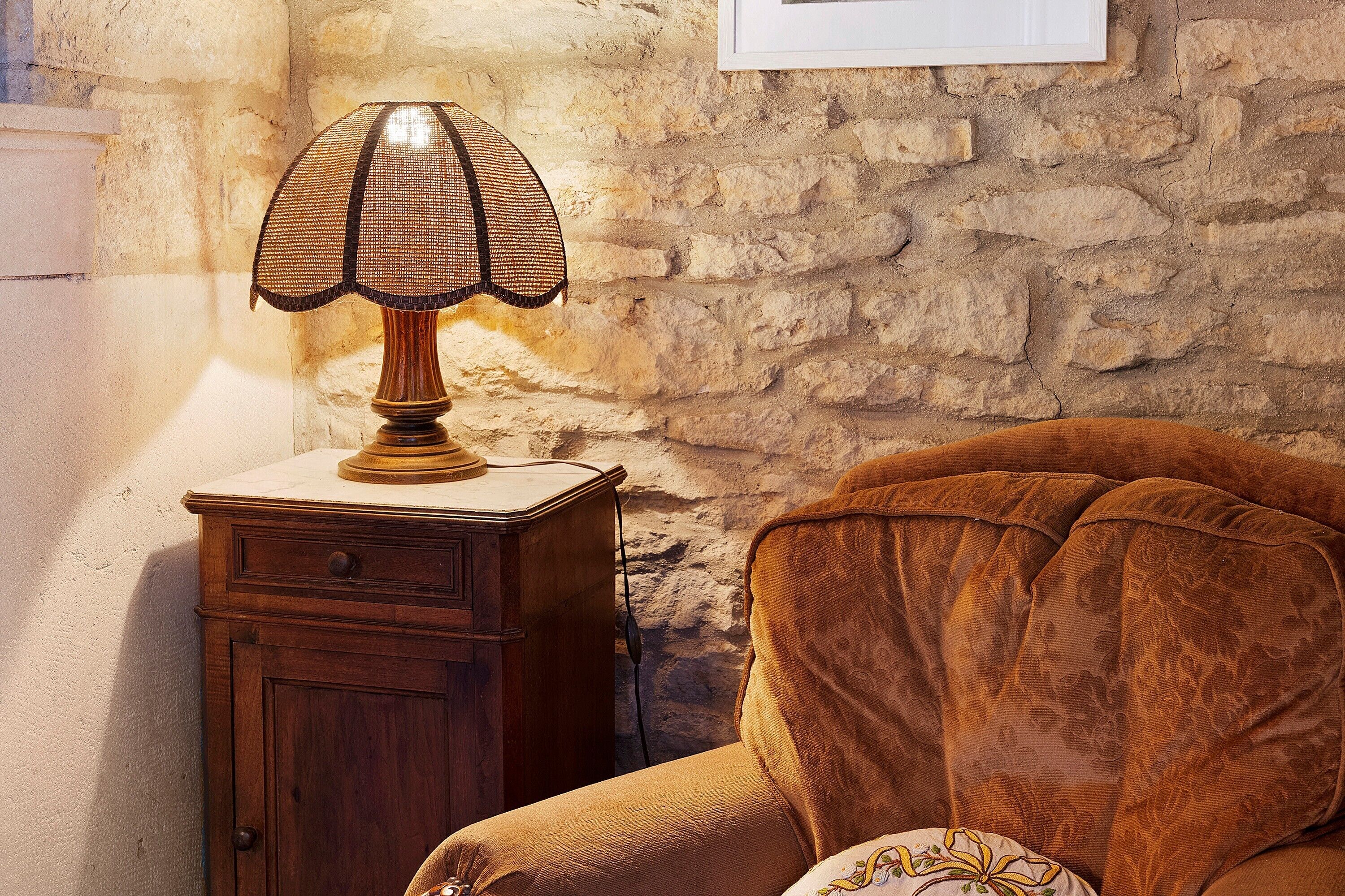 Una habitación con una mesita de noche de madera, una lámpara y un sillón tapizado en marrón.